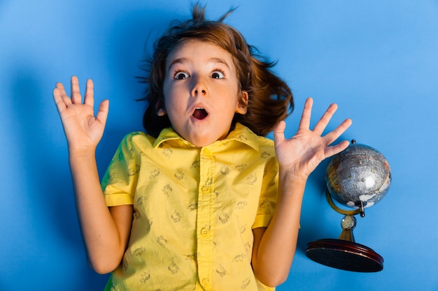 Photo young boy smiling lying on blue background with globe