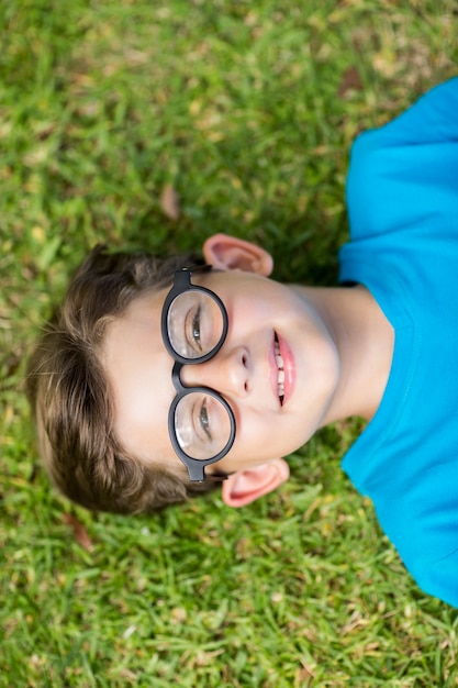 Young boy in spectacle lying on grass