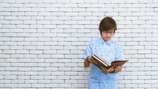 Young boy stand reading book with white brick wall