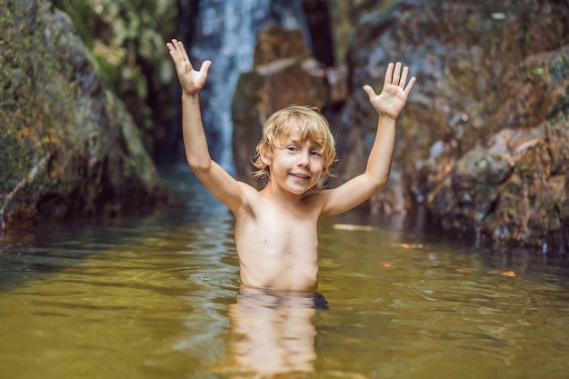 Photo young boy standing in the water at the waterfall