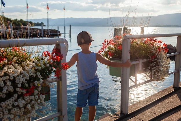 Foto un ragazzino si trova su un molo in un piccolo villaggio sul lago leman circondato da scatole di fiori ornate