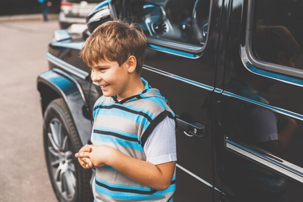 A young boy in a striped sweater stands next to a car