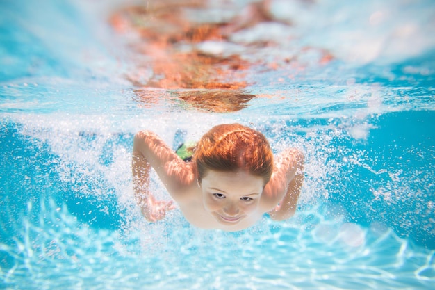 少年は泳ぎ、水泳プールで水中で水中に飛び込みます子供の少年はswimminに飛び込みます