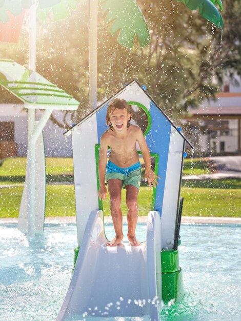 Young boy in swimming trunks standing on deck of pool looking at camera and smiling