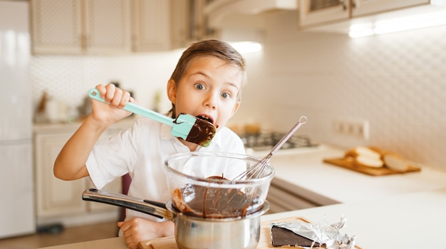 Young boy tastes melted chocolate in a bowl