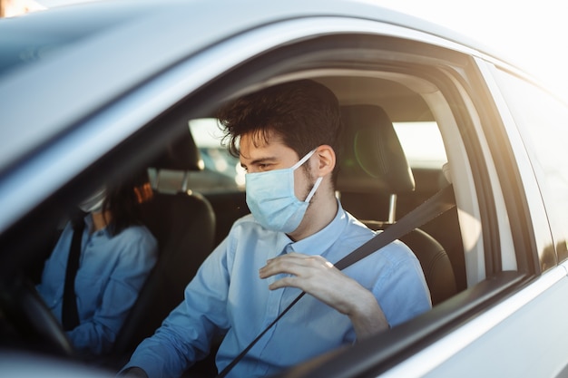 어린 소년 택시 운전사는 멸균 의료 마스크를 착용하고 안전 벨트를 조입니다.