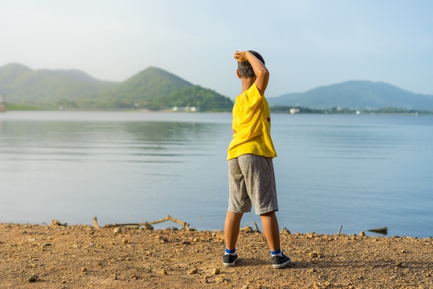 若い男の子が夕日にBang Pra Reservoirの水に石を投げる
