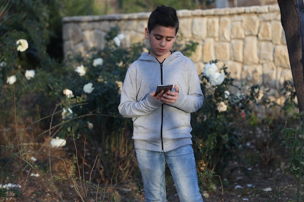 young boy using mobile and takes selfie in park outdoors