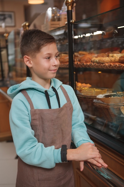 Young boy wearing apron working at his parents bakery store