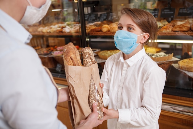 코로나 바이러스 전염병 동안 빵집에서 빵을 사는 의료 얼굴 마스크를 쓰고 어린 소년