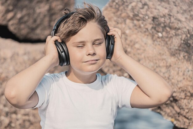 Молодой мальчик в наушниках слушает музыку на открытом воздухе