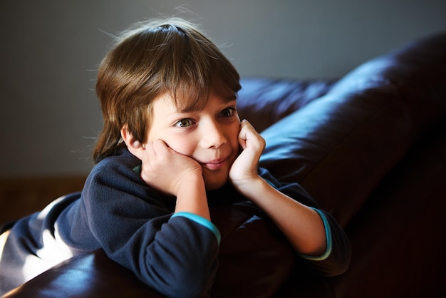 Photo young boy with his hands propping up his head sitting on couch