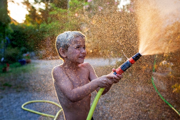 A young boy with joyful laughter sprays water from a garden hose sparkling droplets flying in the