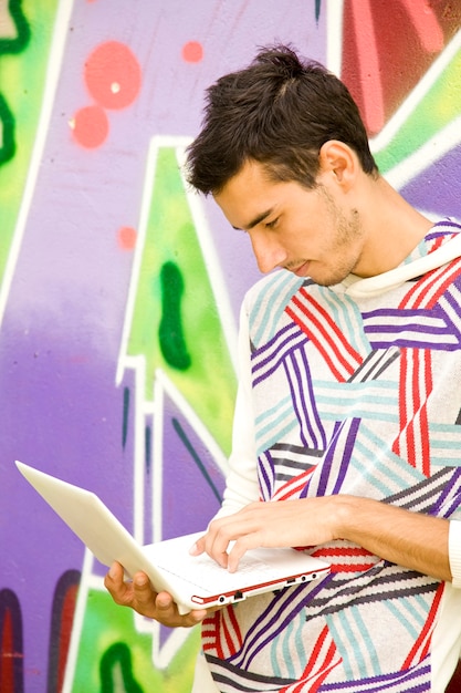 Young boy with laptop near graffiti wall.