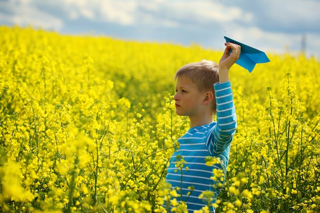 Young boy with paper plane against blue sky and yellow field flo