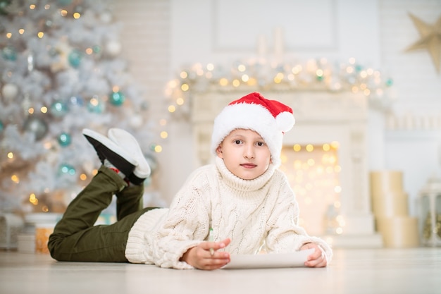 young boy writing a wish list on the floor with christmas decoration in background