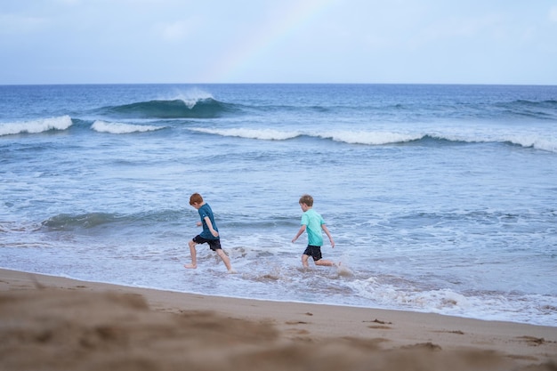 Photo young boys playing in the waves with a rainbow over the ocean on kaanapali beach in hawaii