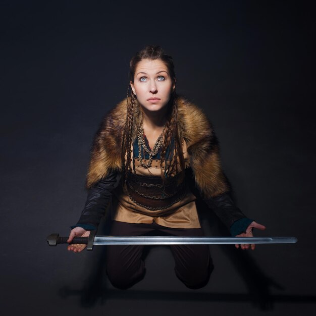 Молодая смелая героиня викингов смотрит на сидящую на полу молодую женщину в скандинавском костюме
