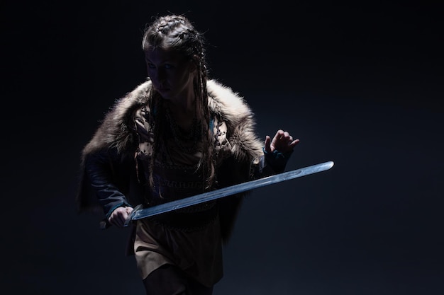 Foto una giovane coraggiosa eroina vichinga con una spada in mano su uno sfondo scuro una giovane donna in abito in s