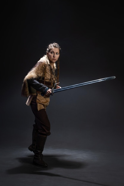 A young brave viking heroine with a sword in hands on a dark background a young woman in a suit in s