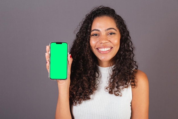 Молодая бразильская чернокожая женщина держит мобильный телефон и показывает рекламное фото на экране