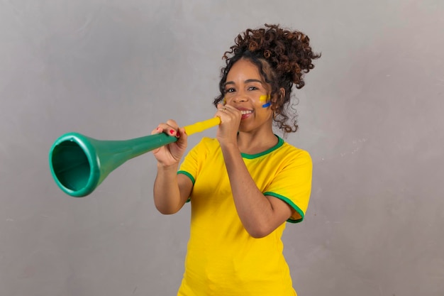 Young brazilian cheerleader with a vuvuzela on grey background celebrating