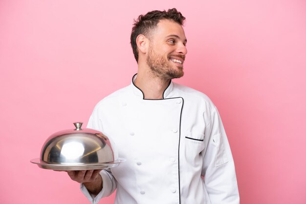 Young Brazilian chef with tray isolated on pink background looking side