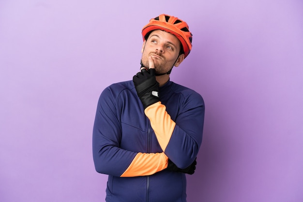 Young Brazilian cyclist man isolated on purple background having doubts while looking up