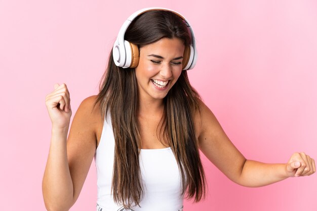 Young brazilian girl isolated on pink listening music and dancing