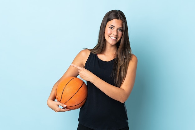 Young Brazilian girl isolated playing basketball and pointing to the lateral