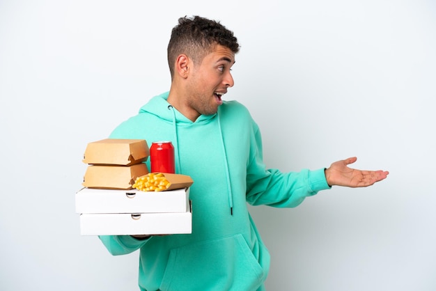 Young Brazilian holding fast food isolated on white background with surprise expression while looking side