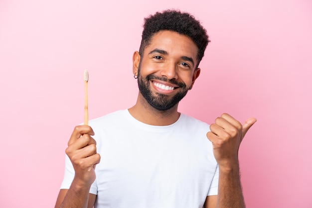 Young Brazilian man brushing teeth isolated on pink background pointing to the side to present a product