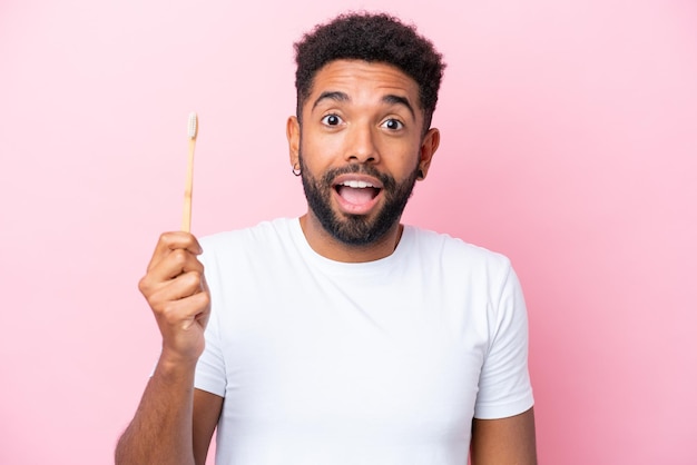 Young Brazilian man brushing teeth isolated on pink background with surprise and shocked facial expression