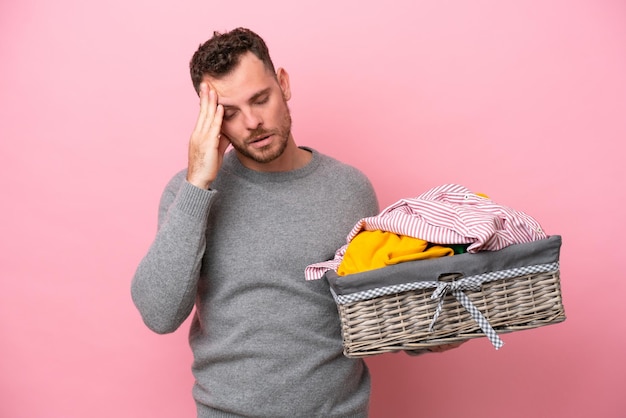 Young Brazilian man holding a clothes basket isolated on pink background with headache