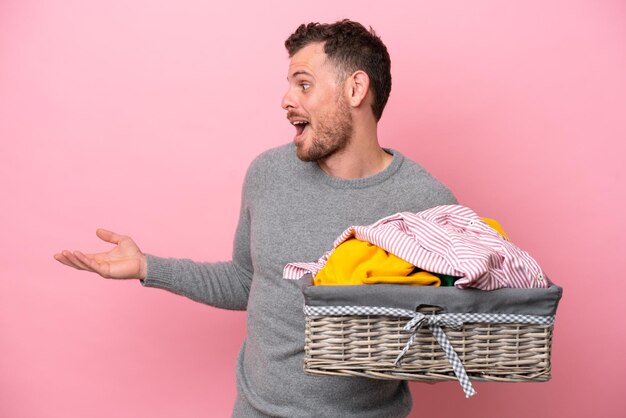 Young brazilian man holding a clothes basket isolated on pink background with surprise expression while looking side