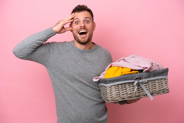 Young Brazilian man holding a clothes basket isolated on pink background with surprise expression