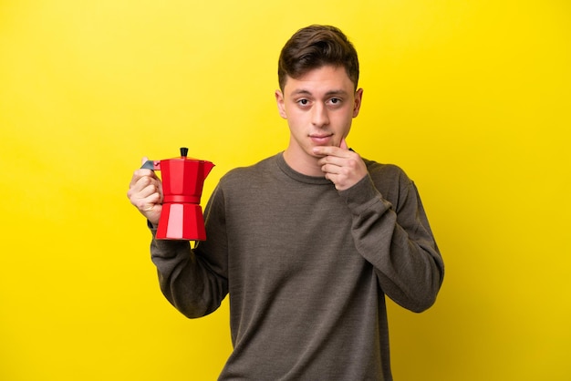 Молодой бразилец держит кофейник на желтом фоне и думает