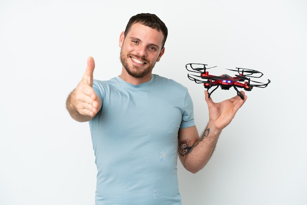 Young Brazilian man holding a drone isolated on white background shaking hands for closing a good deal