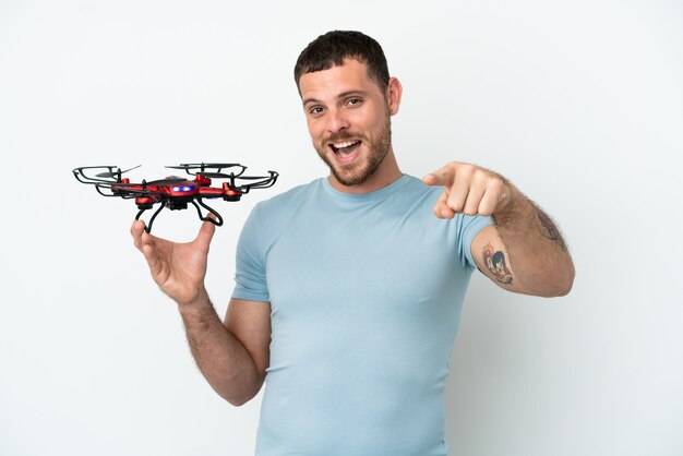 Young Brazilian man holding a drone isolated on white background surprised and pointing front