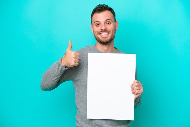 Young Brazilian man holding an empty placard isolated on blue background holding an empty placard with thumb up