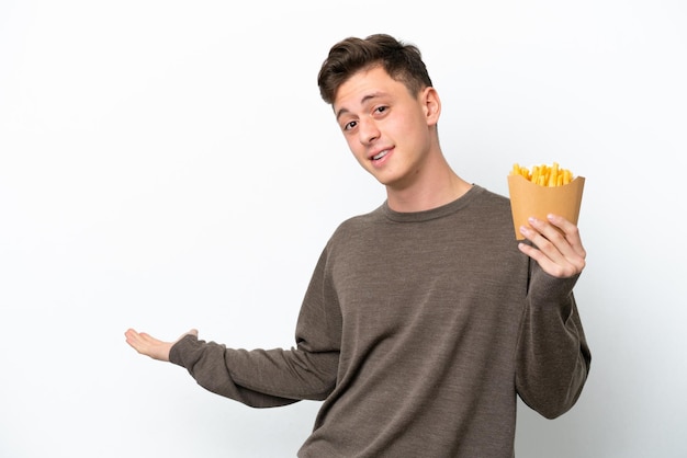 Young Brazilian man holding fried chips isolated on white background extending hands to the side for inviting to come