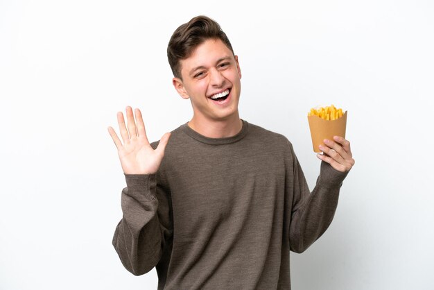 Young Brazilian man holding fried chips isolated on white background saluting with hand with happy expression