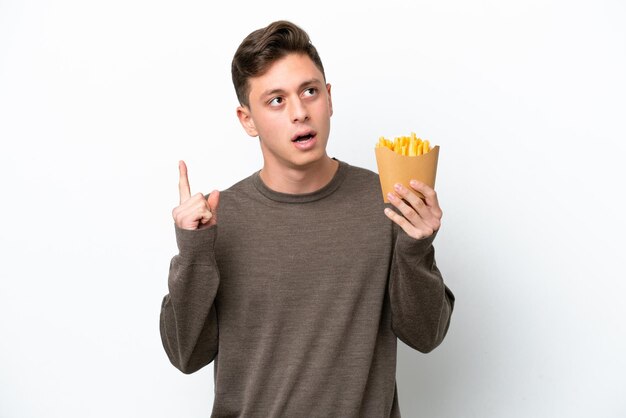 Giovane uomo brasiliano che tiene patatine fritte isolate su sfondo bianco pensando a un'idea che punta il dito verso l'alto