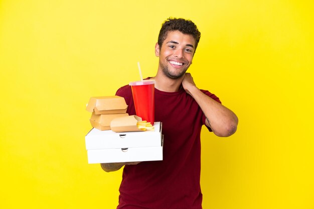 Young brazilian man holding pizzas and burgers isolated background laughing