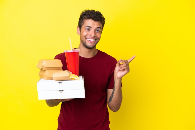 Il giovane brasiliano che tiene le pizze e gli hamburger ha isolato lo sfondo che indica il lato per presentare un prodotto