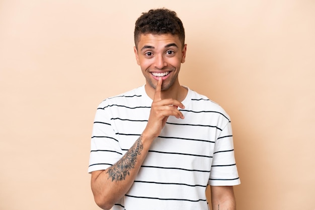 Young Brazilian man isolated on beige background showing a sign of silence gesture putting finger in mouth