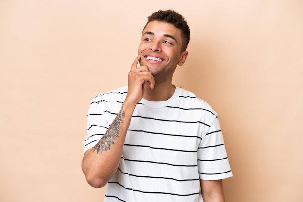 Young Brazilian man isolated on beige background thinking an idea while looking up