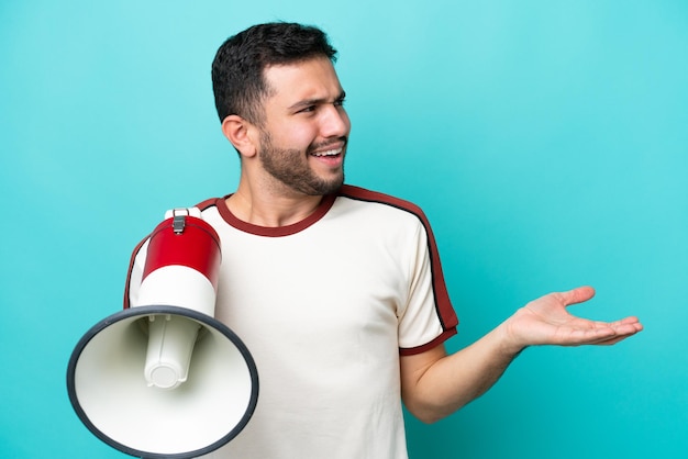 Young Brazilian man isolated on blue background holding a megaphone and with surprise facial expression