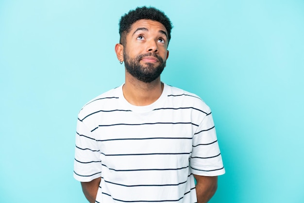 Young Brazilian man isolated on blue background and looking up