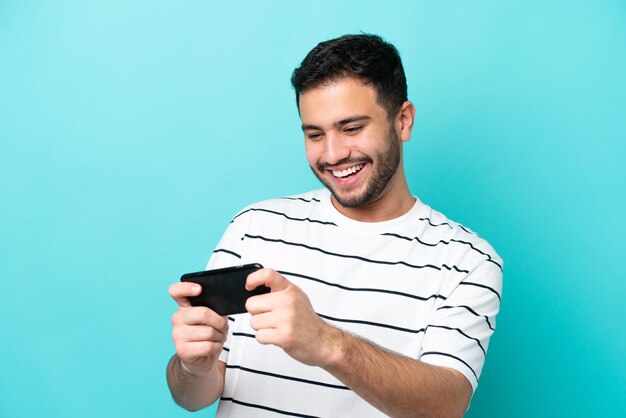 Young Brazilian man isolated on blue background playing with the mobile phone